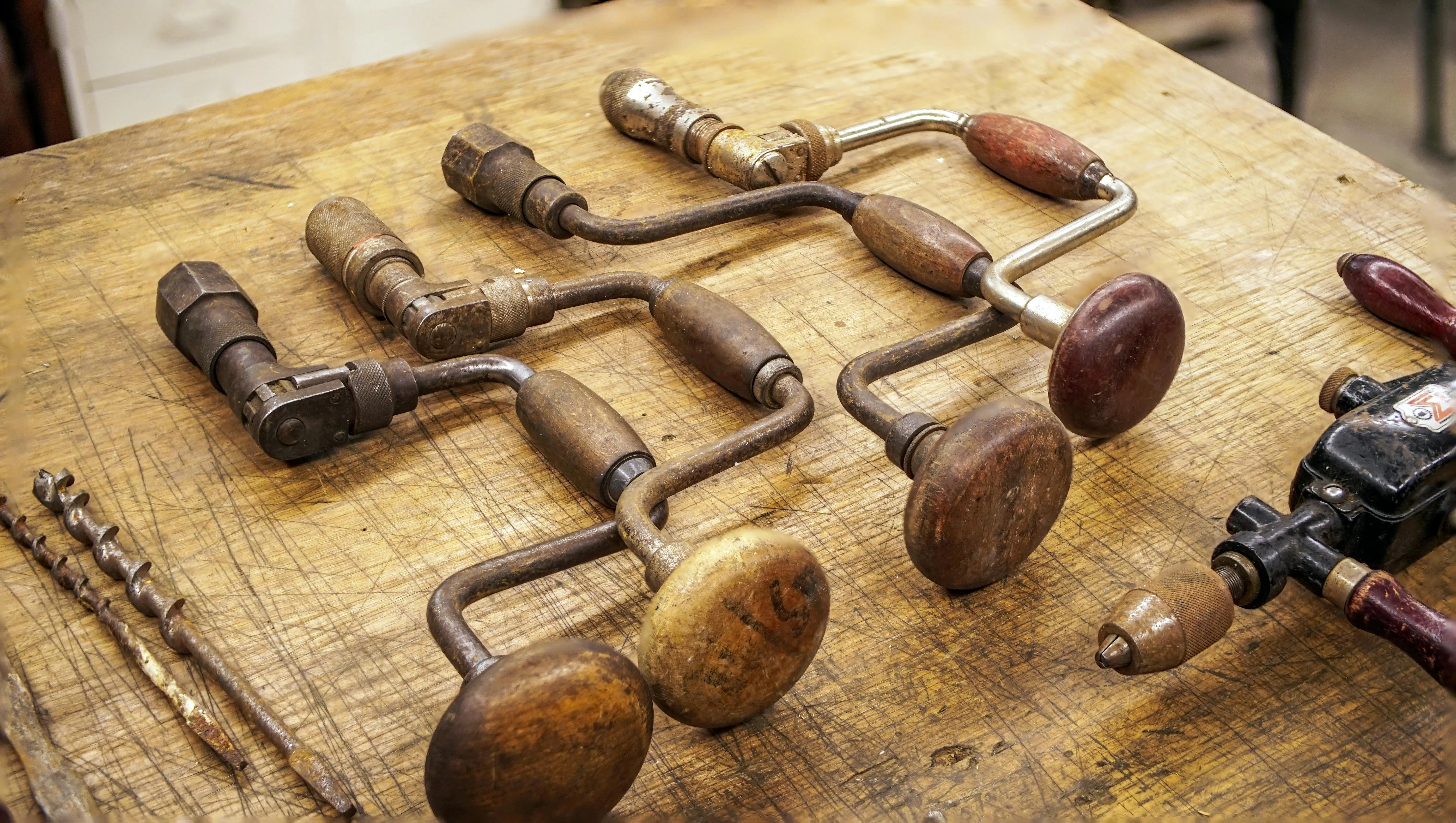 Collection of vintage and antique tools including old planes, braces, and hand saws laid out on aged wood
